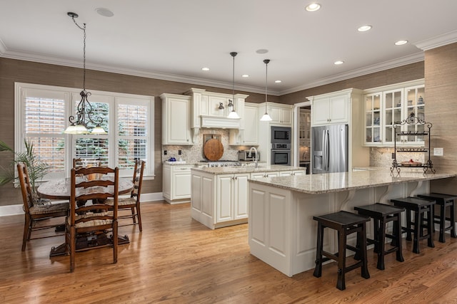 kitchen featuring light wood-type flooring, stainless steel appliances, decorative light fixtures, and light stone countertops