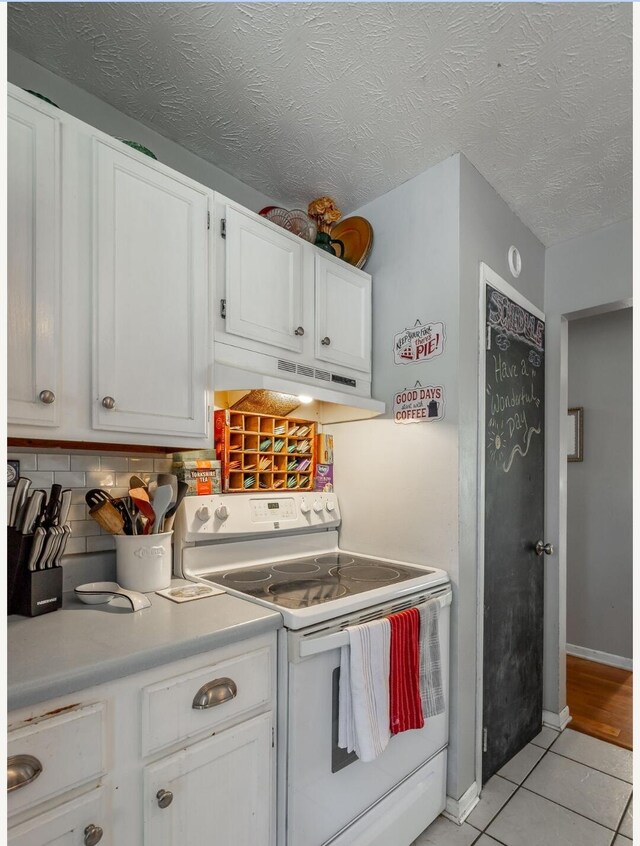 kitchen featuring white cabinets, tasteful backsplash, light tile patterned floors, a textured ceiling, and white range with electric stovetop