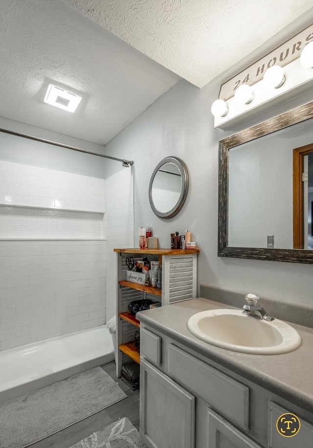 bathroom with vanity, tiled shower, a textured ceiling, and wood-type flooring