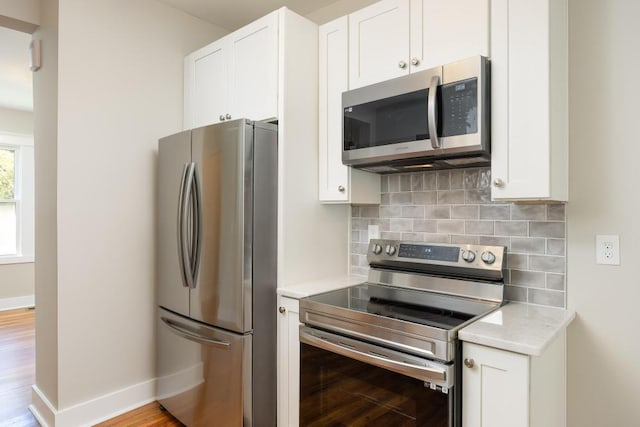 kitchen with decorative backsplash, appliances with stainless steel finishes, white cabinetry, and light hardwood / wood-style floors