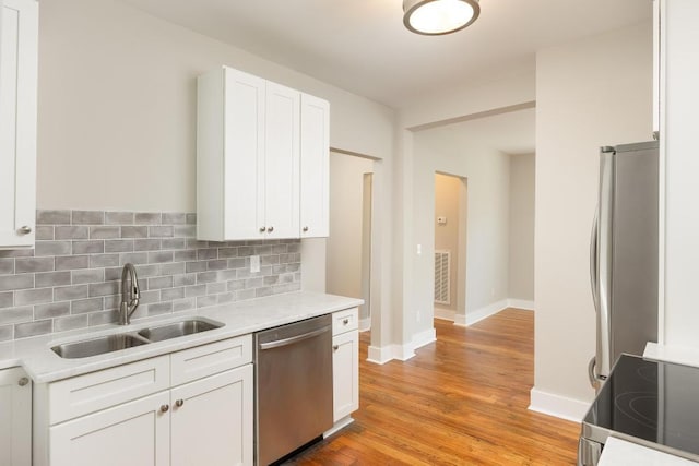 kitchen featuring sink, light wood-type flooring, backsplash, white cabinetry, and stainless steel appliances