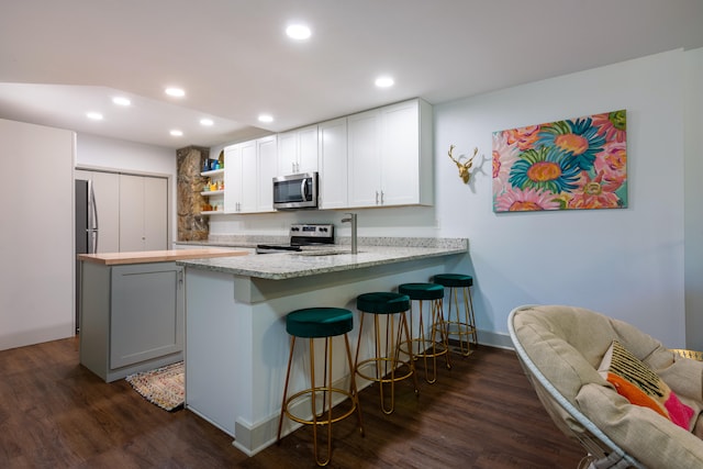 kitchen with white cabinetry, appliances with stainless steel finishes, kitchen peninsula, and dark wood-type flooring