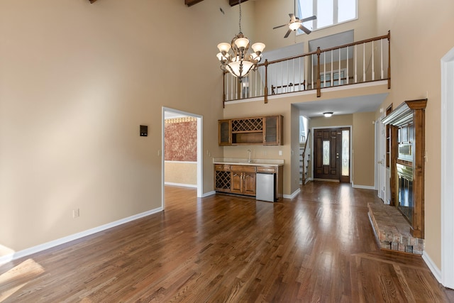 unfurnished living room with sink, a high ceiling, dark wood-type flooring, and ceiling fan with notable chandelier