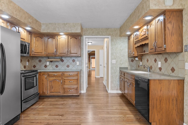 kitchen with stainless steel appliances, sink, light wood-type flooring, and backsplash