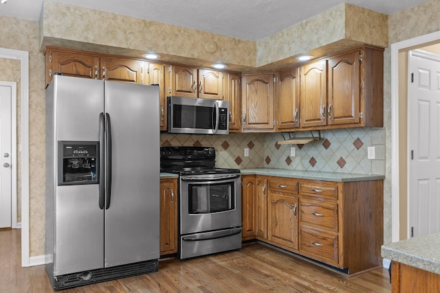 2508 Lake Dweller Ln, Hixson, TN 37343 - kitchen with appliances with stainless steel finishes, brown cabinetry, light wood finished floors, light countertops, and decorative backsplash