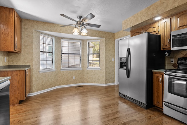 kitchen with a textured ceiling, hardwood / wood-style flooring, stainless steel appliances, and ceiling fan