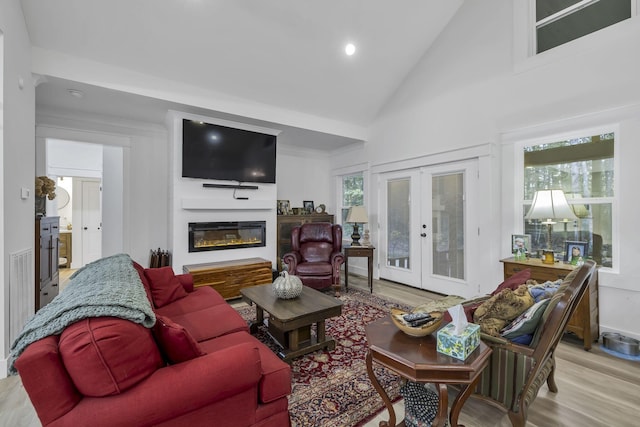 living room with french doors, light hardwood / wood-style floors, high vaulted ceiling, and a healthy amount of sunlight