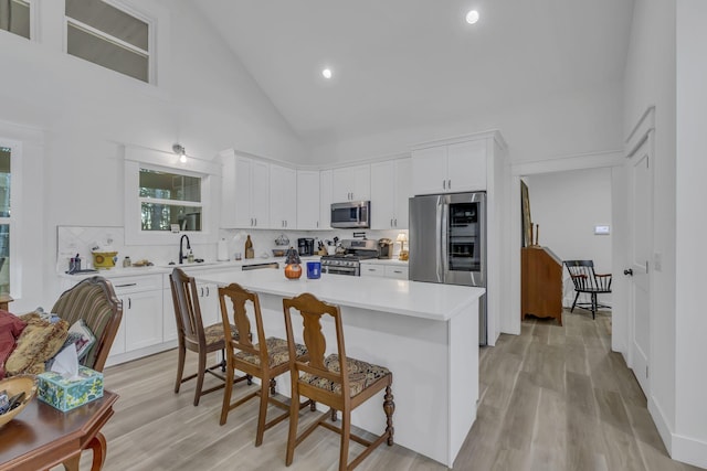 kitchen with a kitchen island, a kitchen breakfast bar, stainless steel appliances, white cabinetry, and high vaulted ceiling