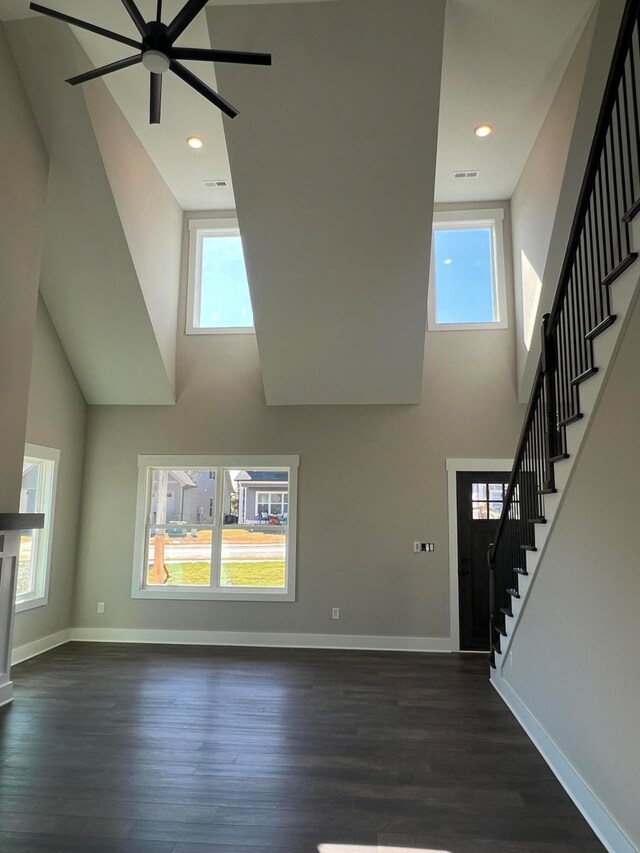 unfurnished living room with a towering ceiling, dark wood-type flooring, and ceiling fan