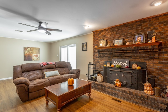living room with ceiling fan, wood-type flooring, ornamental molding, and a brick fireplace