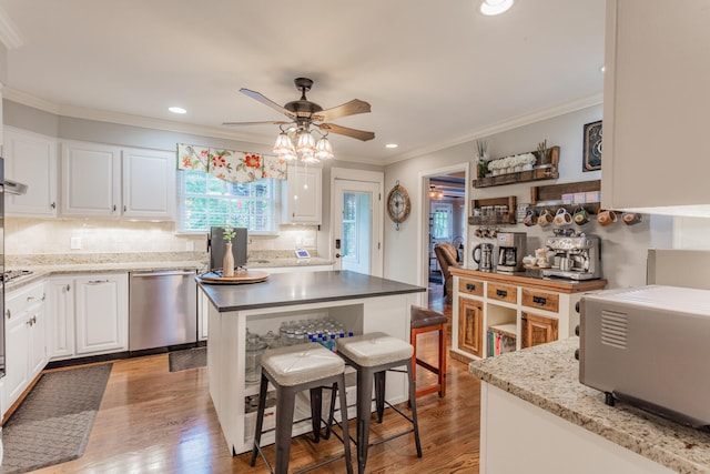 kitchen featuring a center island, white cabinetry, stainless steel dishwasher, crown molding, and hardwood / wood-style flooring