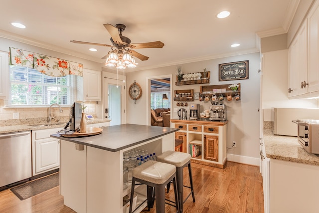 kitchen featuring a breakfast bar area, white cabinetry, stainless steel dishwasher, crown molding, and light hardwood / wood-style flooring