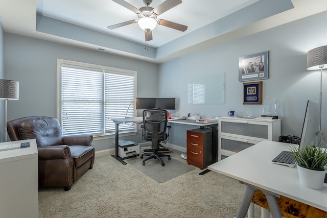 carpeted office featuring ceiling fan and a tray ceiling