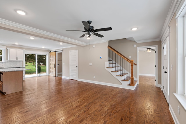 unfurnished living room with hardwood / wood-style floors, a barn door, ceiling fan, and crown molding