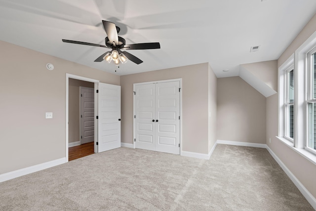 unfurnished bedroom featuring ceiling fan, multiple windows, light carpet, and a closet