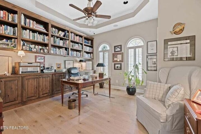 office area featuring ceiling fan, light hardwood / wood-style floors, and a raised ceiling