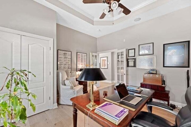 office space with ceiling fan, a tray ceiling, ornamental molding, a high ceiling, and light hardwood / wood-style floors