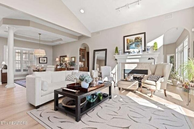 living room featuring lofted ceiling, a notable chandelier, ornate columns, and light wood-type flooring