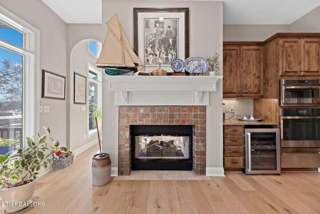 bar featuring light hardwood / wood-style flooring, wine cooler, a tile fireplace, and stainless steel oven