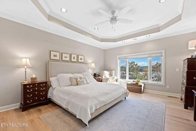 bedroom featuring ceiling fan, ornamental molding, a tray ceiling, and light wood-type flooring