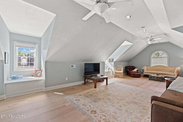 living room with light hardwood / wood-style floors, lofted ceiling with skylight, a healthy amount of sunlight, and ceiling fan