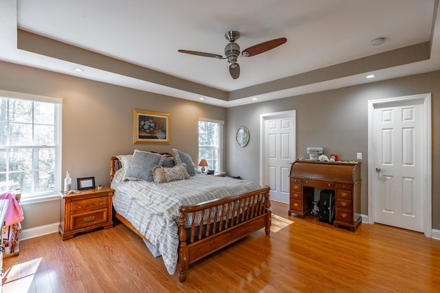 bedroom with light wood-type flooring, a tray ceiling, and ceiling fan