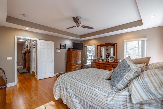 bedroom featuring a raised ceiling, a walk in closet, light hardwood / wood-style flooring, and ceiling fan