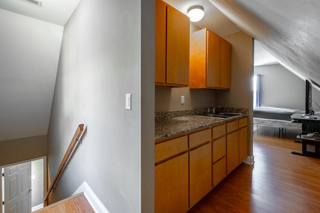 kitchen with dark stone counters, a textured ceiling, sink, dark hardwood / wood-style floors, and lofted ceiling