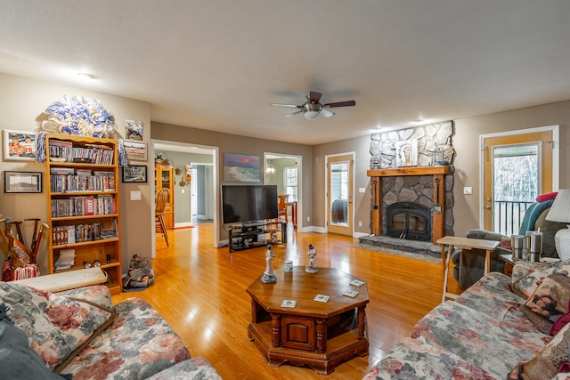 living room with a wealth of natural light, ceiling fan, light wood-type flooring, and a stone fireplace