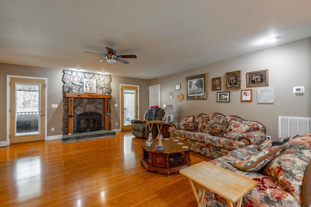 living room with a stone fireplace, ceiling fan, and wood-type flooring