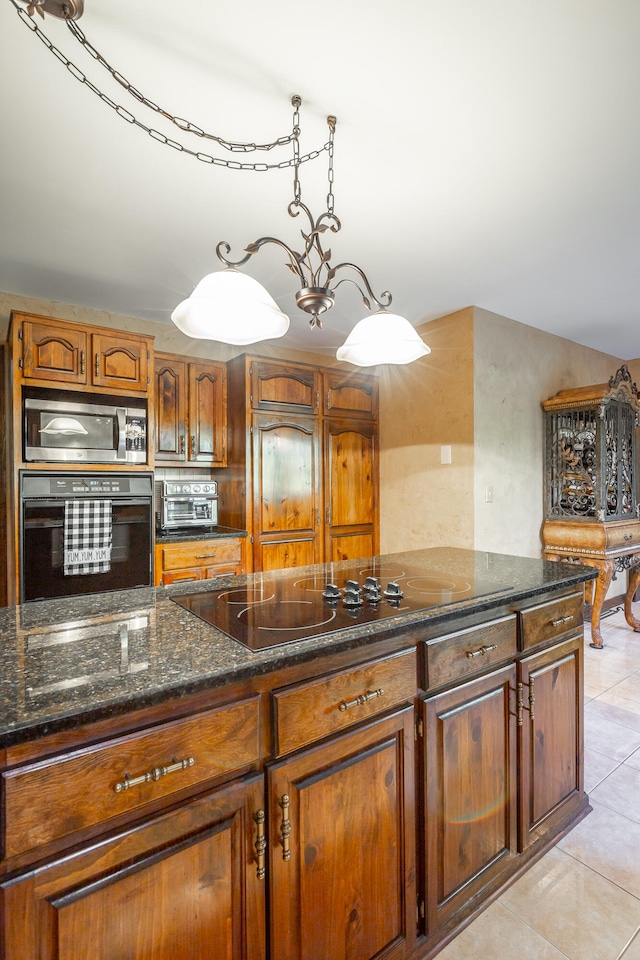 kitchen featuring stainless steel microwave, oven, dark stone counters, a notable chandelier, and light tile patterned floors