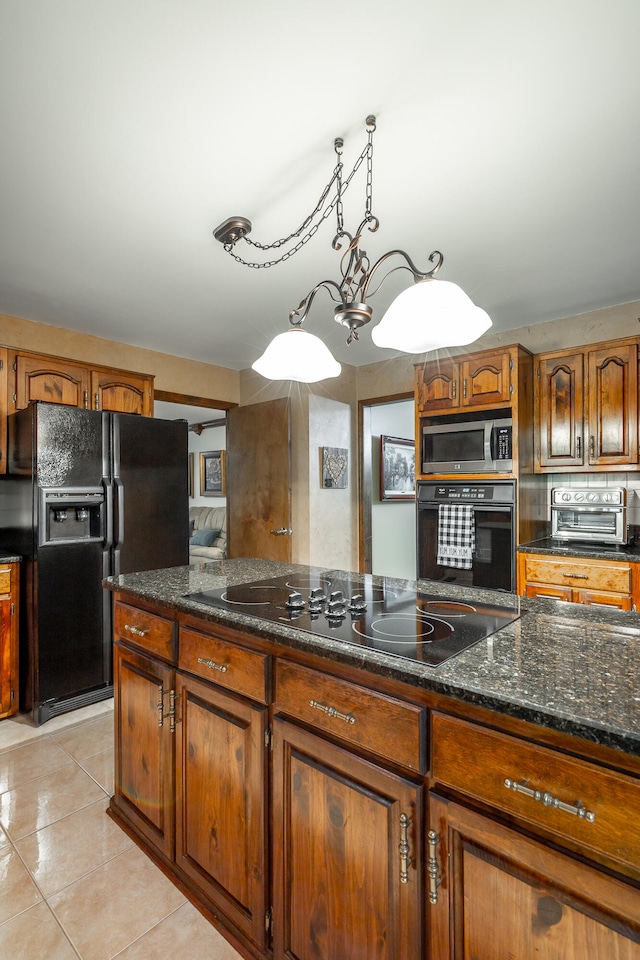 kitchen with dark stone counters, light tile patterned flooring, black appliances, pendant lighting, and a notable chandelier