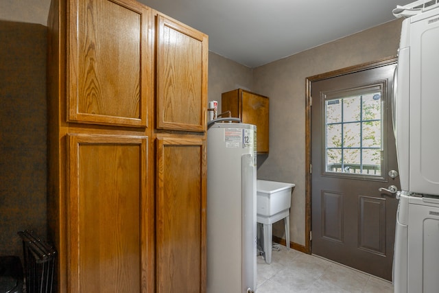 clothes washing area featuring stacked washing maching and dryer, cabinets, water heater, and light tile patterned floors