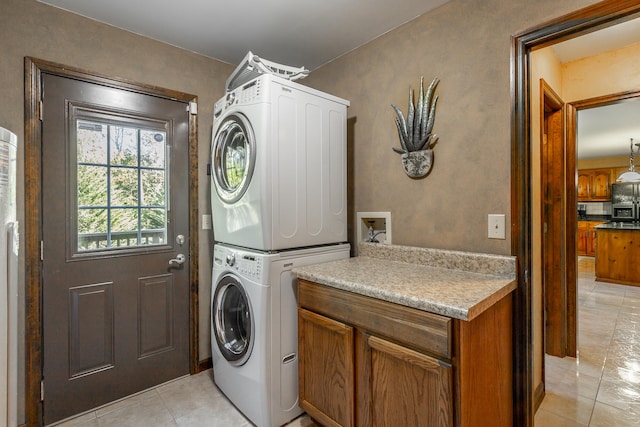 laundry room featuring light tile patterned flooring, cabinets, and stacked washing maching and dryer