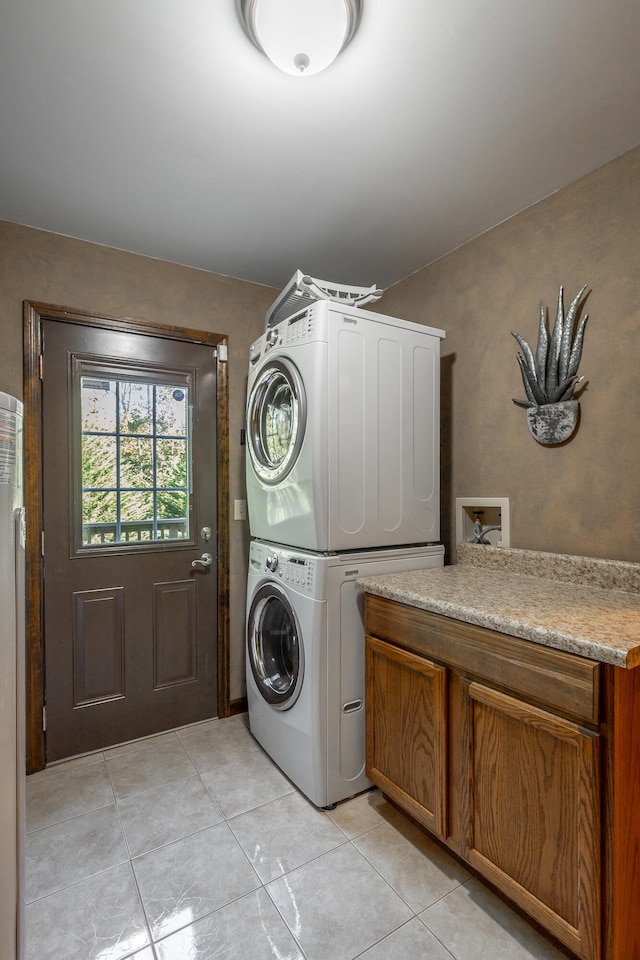 laundry room featuring cabinets, light tile patterned flooring, and stacked washer and clothes dryer