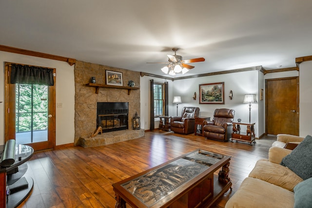 living room featuring ceiling fan, hardwood / wood-style flooring, ornamental molding, and a stone fireplace