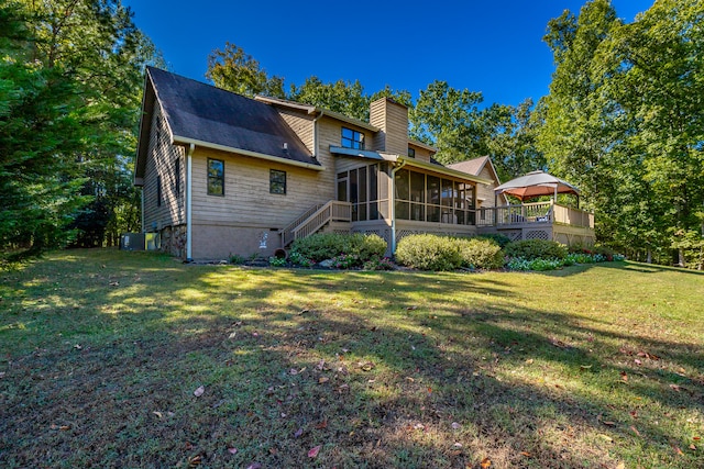 rear view of property featuring a deck, a lawn, and a sunroom