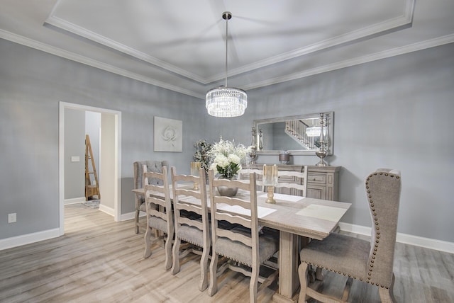 dining room featuring a raised ceiling, light wood-type flooring, and ornamental molding