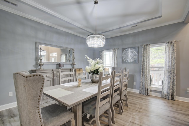 dining area featuring a chandelier, ornamental molding, light hardwood / wood-style flooring, and a tray ceiling