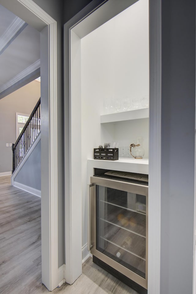 bar with light hardwood / wood-style flooring, beverage cooler, and ornamental molding