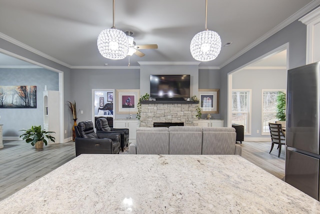 interior space with ceiling fan with notable chandelier, light wood-type flooring, ornamental molding, and a fireplace