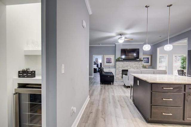 kitchen with light stone countertops, ceiling fan, wine cooler, a stone fireplace, and pendant lighting