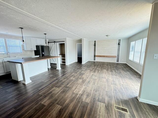 unfurnished living room with a sink, a barn door, visible vents, dark wood-style floors, and baseboards