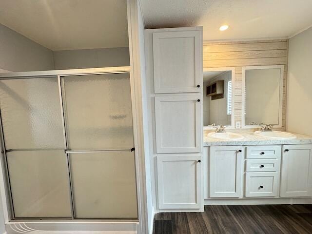 bathroom featuring double vanity, wood finished floors, a stall shower, and a sink