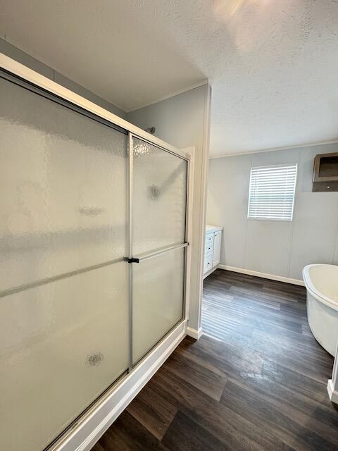 bathroom featuring wood finished floors, baseboards, a stall shower, a textured ceiling, and a soaking tub