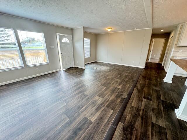 unfurnished living room with a textured ceiling, baseboards, and dark wood-type flooring
