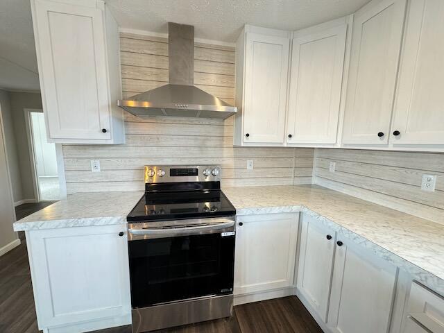 kitchen featuring dark wood finished floors, stainless steel electric range oven, light countertops, wall chimney range hood, and white cabinetry