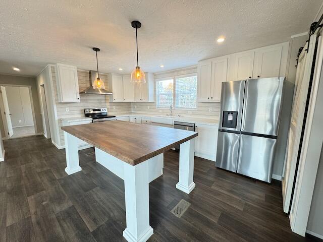 kitchen featuring a sink, white cabinetry, wall chimney range hood, wooden counters, and appliances with stainless steel finishes
