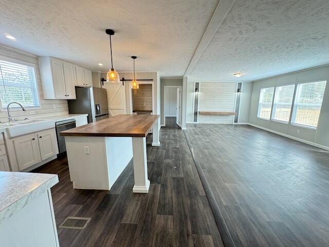 kitchen featuring stainless steel fridge with ice dispenser, wooden counters, a sink, a textured ceiling, and dishwashing machine