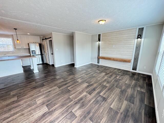 unfurnished living room featuring baseboards, a barn door, a textured ceiling, and dark wood-style flooring